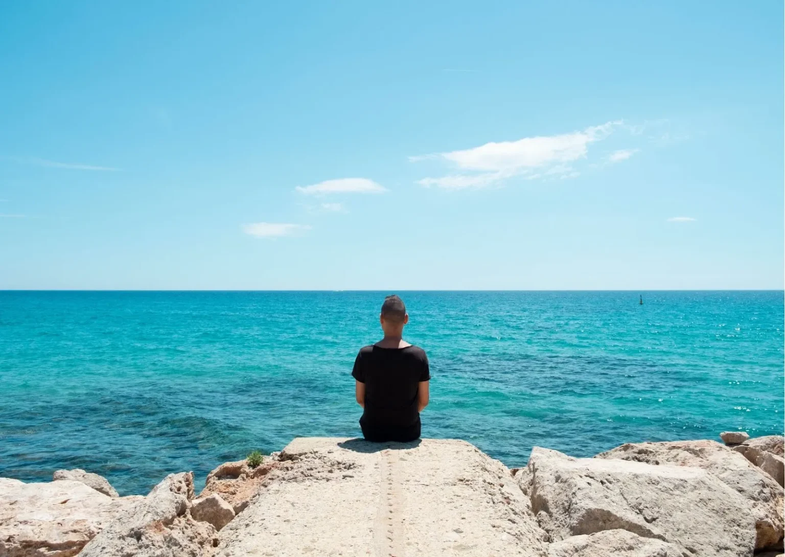hombre sentado en una piedra frente al mar